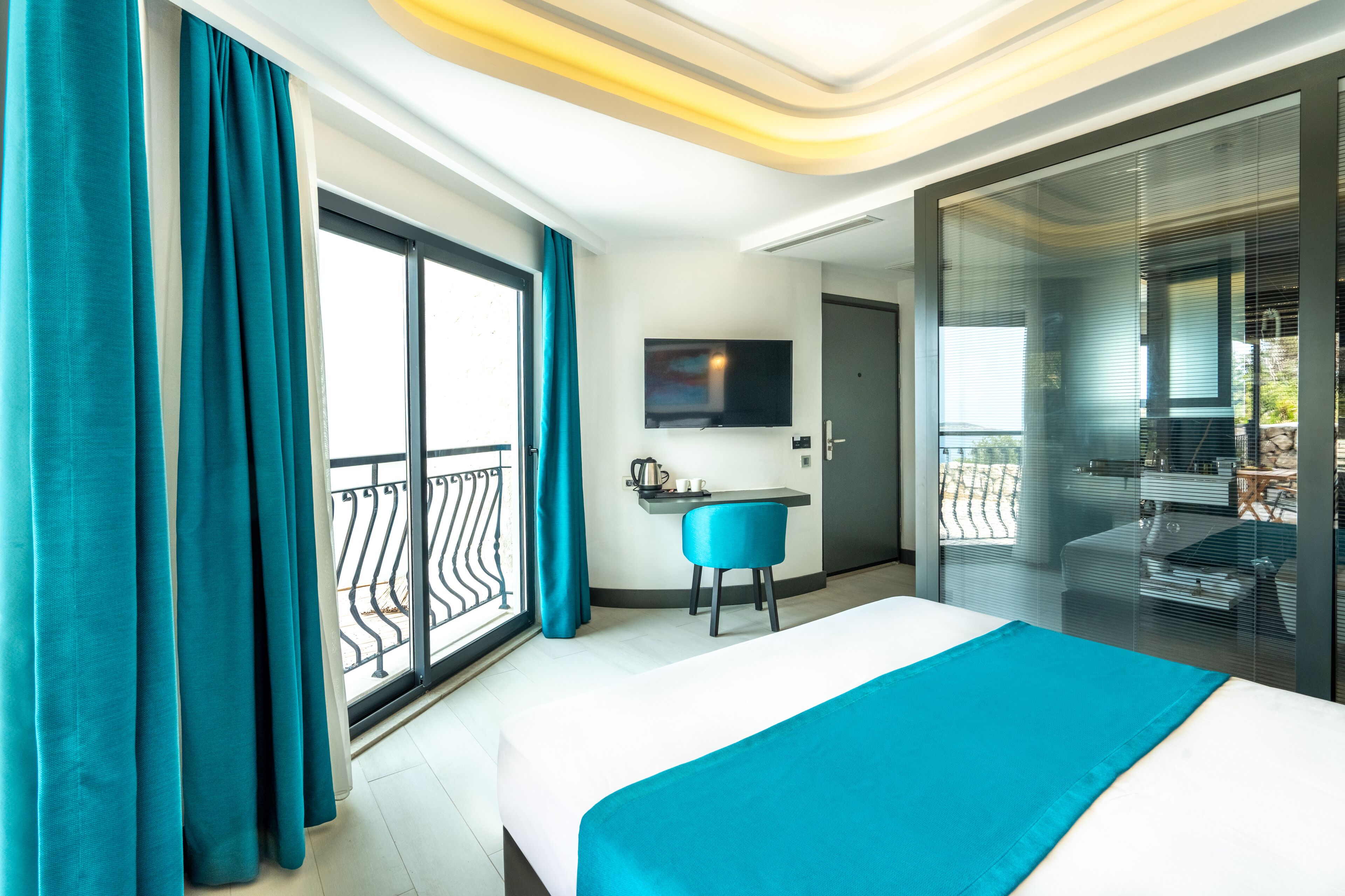 A modern hotel room with a large bed, a desk with a chair, a flat-screen TV, and a balcony with a glass door.