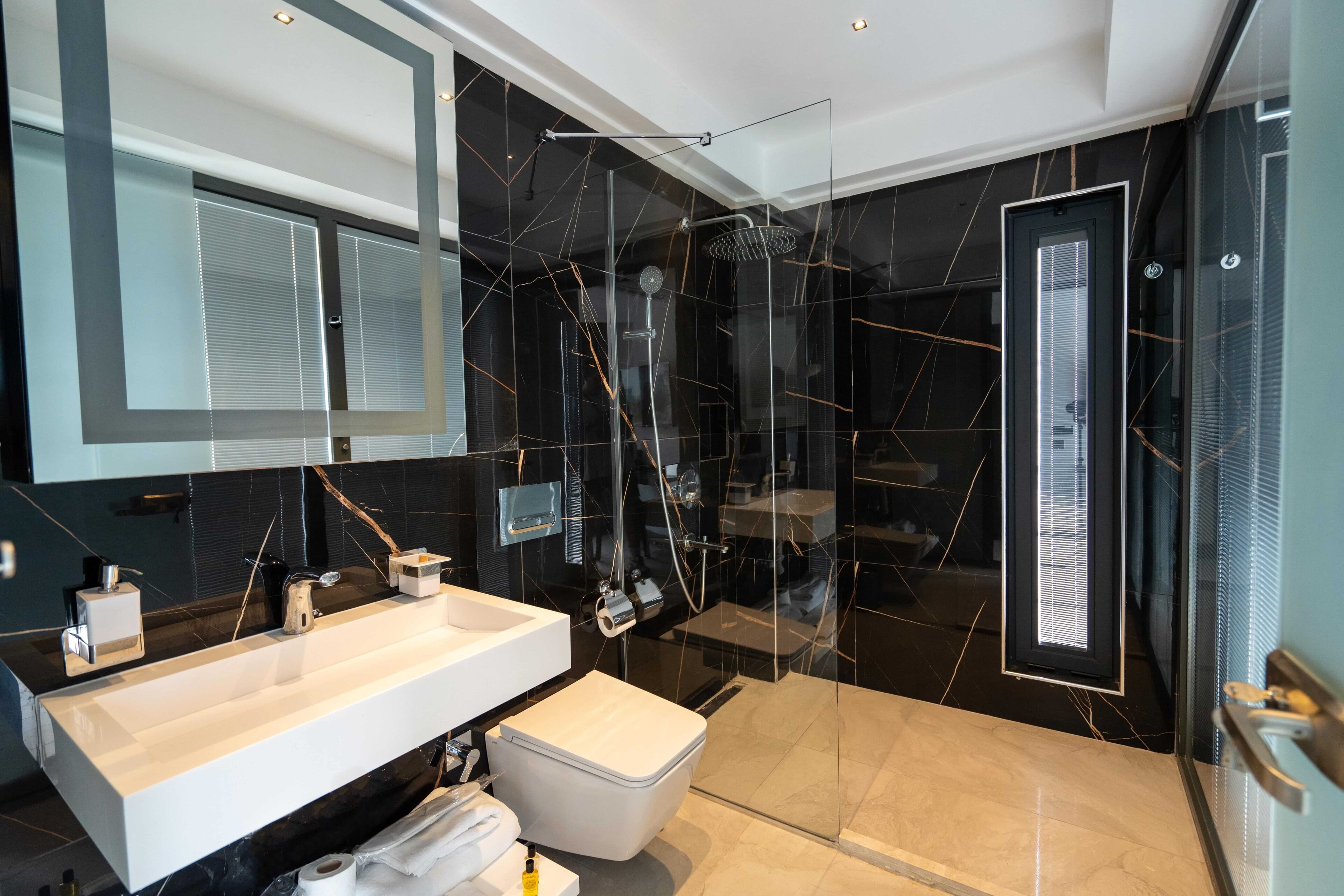 A modern bathroom with a large mirror, dual sinks, a toilet, and a glass-enclosed shower area.