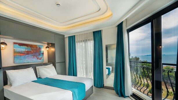 A modern hotel room with a large bed, a view of the sea, and a balcony with a railing. - GÜMÜŞ YAZAR  HOTEL (Kas)