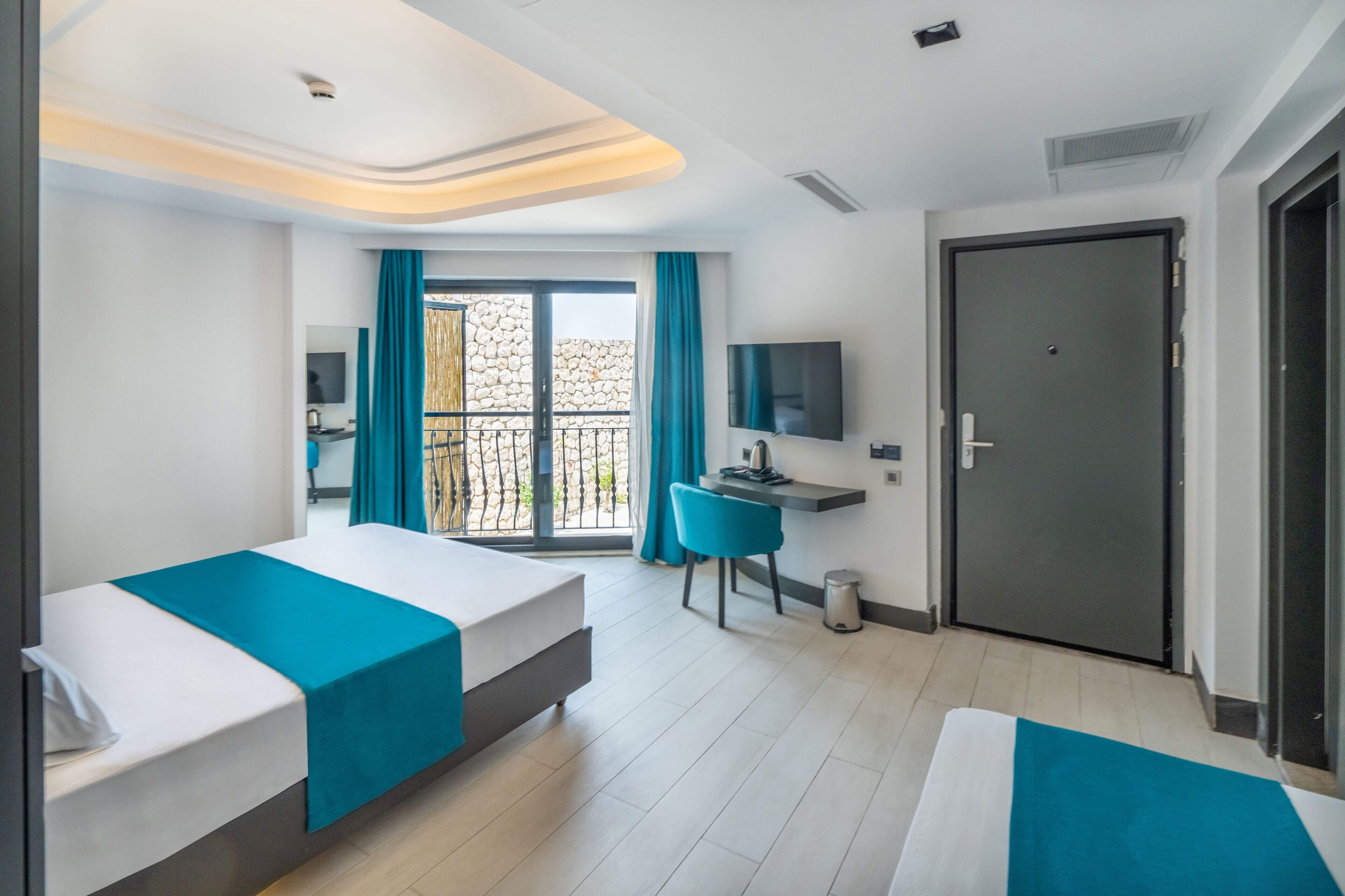 Habitación de hotel con dos camas, un escritorio, un televisor y un balcón con cortinas.