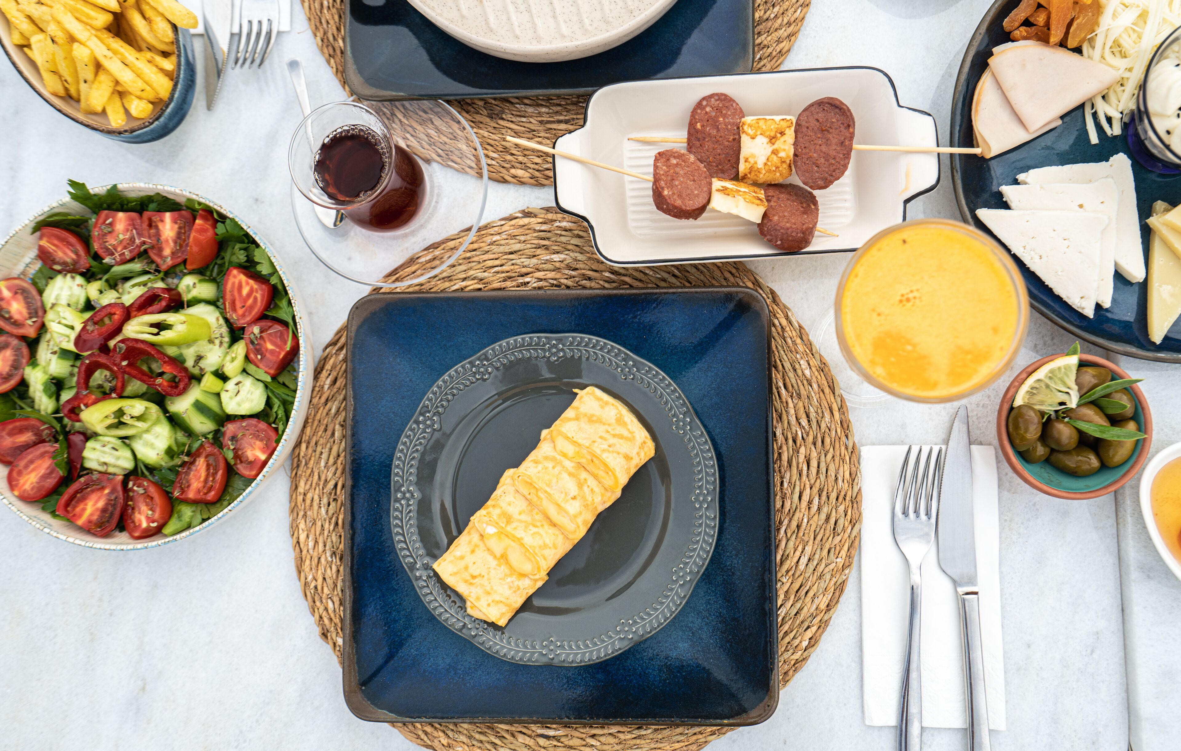 A table with a variety of food items including a salad, cheese, and a rolled pastry.