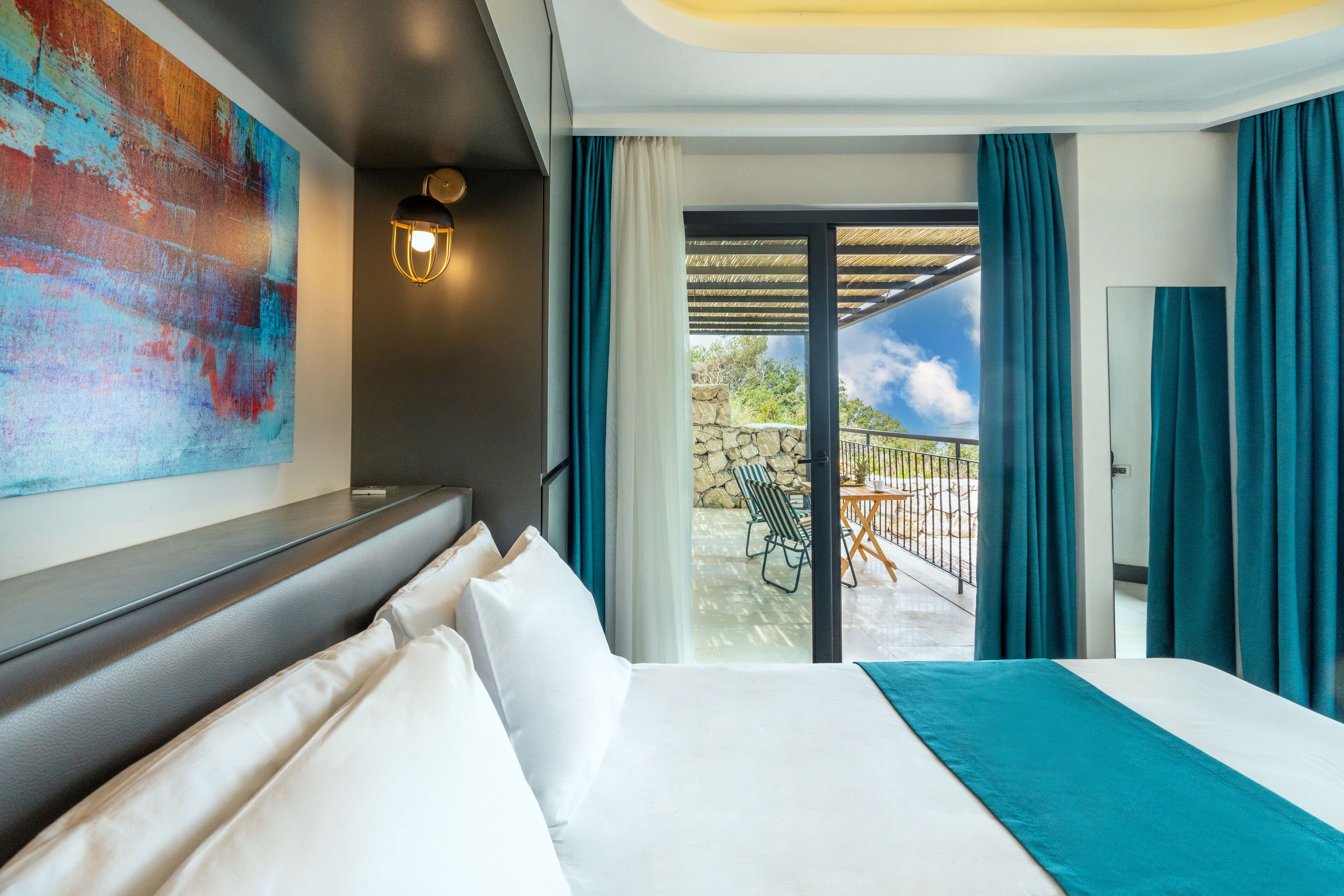A hotel room with a large bed, a view of the outdoor patio, and a colorful abstract painting on the wall.