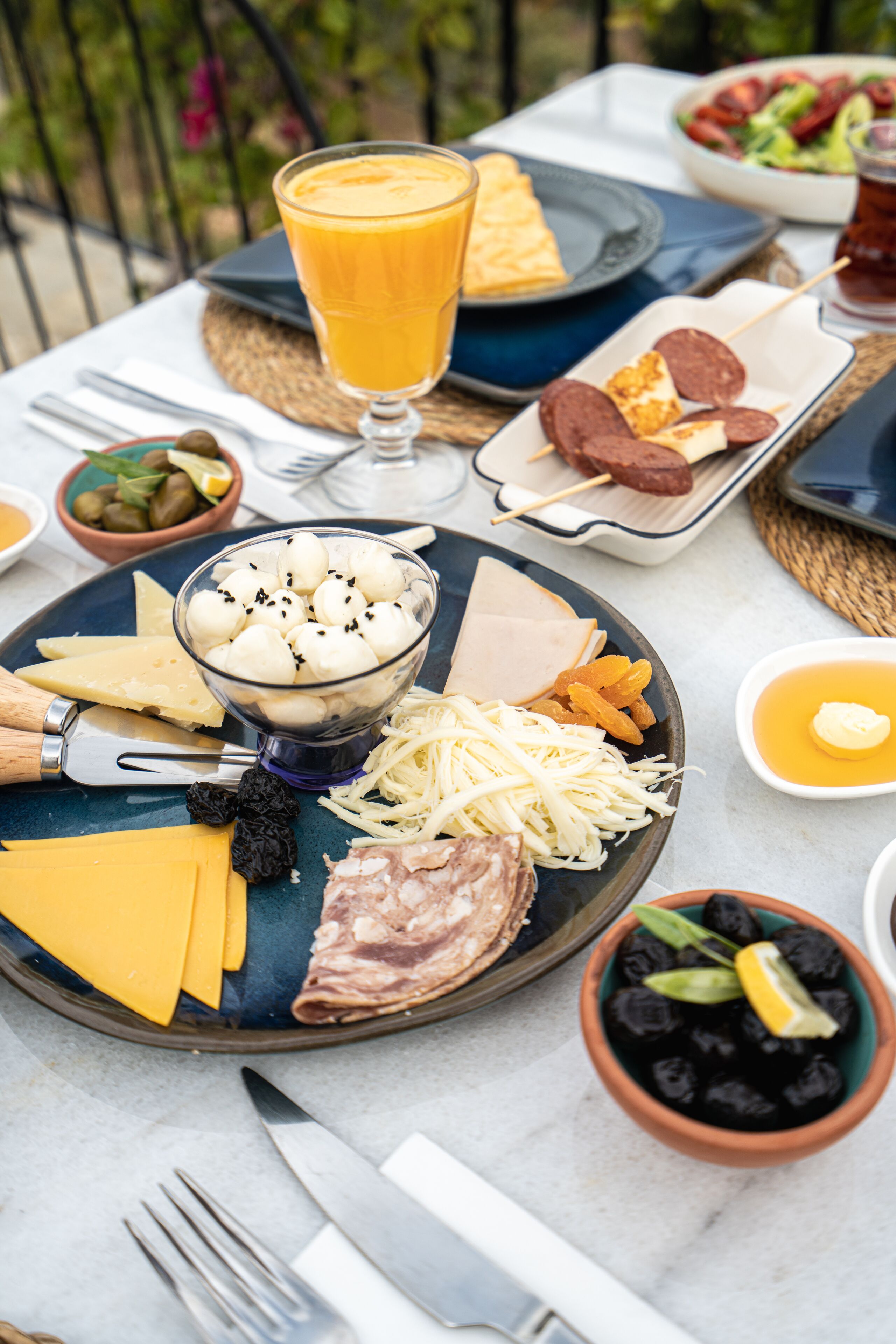 A table set with a variety of foods including cheese, meats, and olives, with a glass of orange juice.