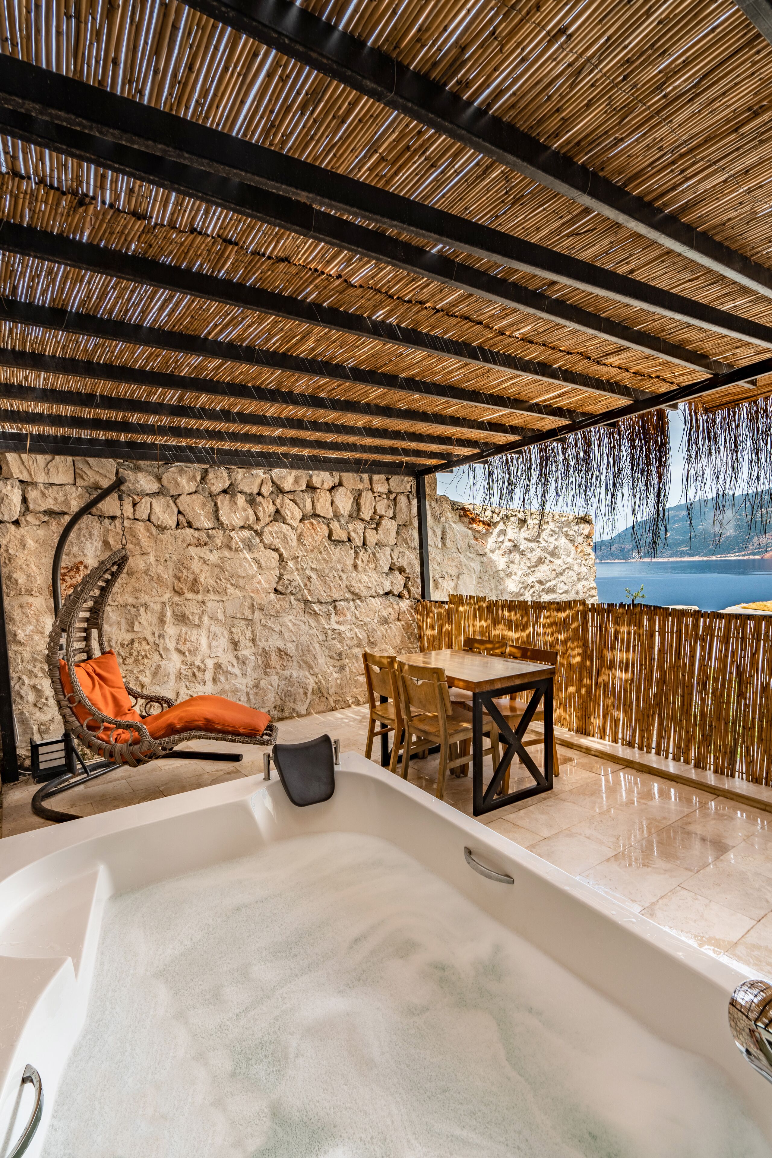 Zona de spa con jacuzzi, sillones de mimbre y una pared de piedra.