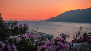 A sunset view over a calm lake with mountains in the background and purple flowers in the foreground. - GÜMÜŞ YAZAR  HOTEL (Kas)