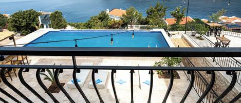 A pool with a view of the sea, a balcony with a railing, and outdoor seating.