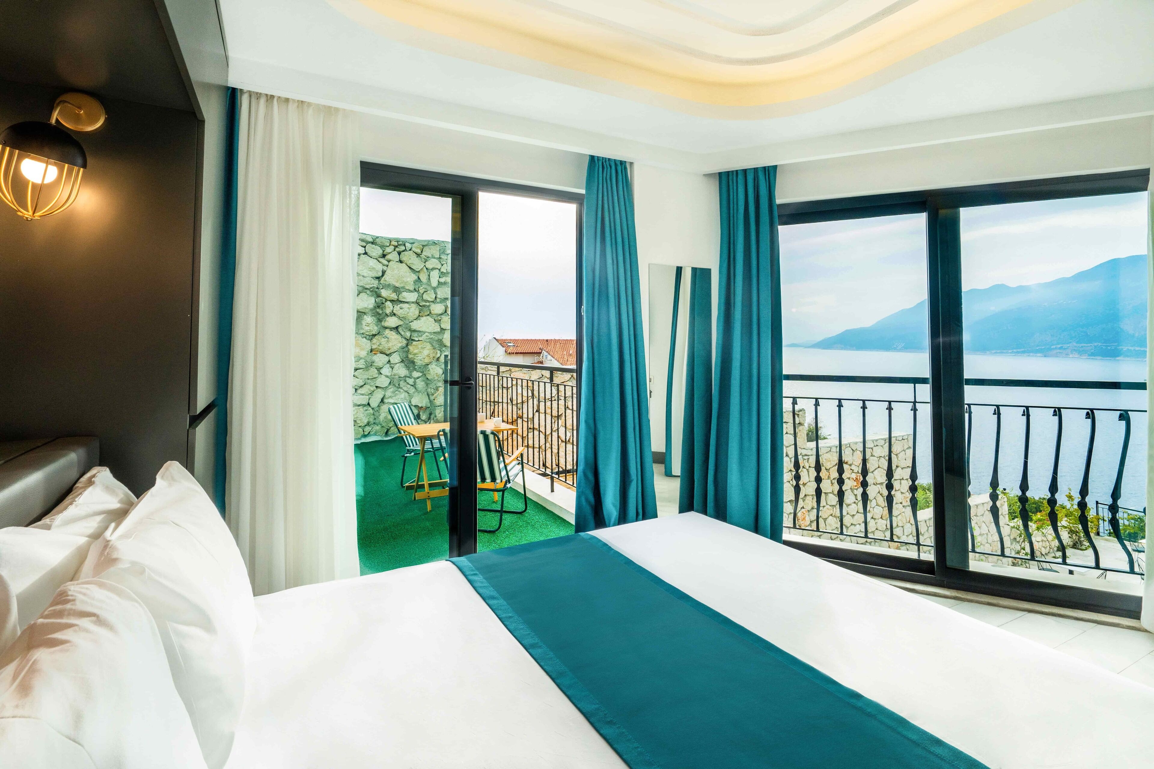 A hotel room with a large bed, a balcony with a view of the sea, and a stone wall.