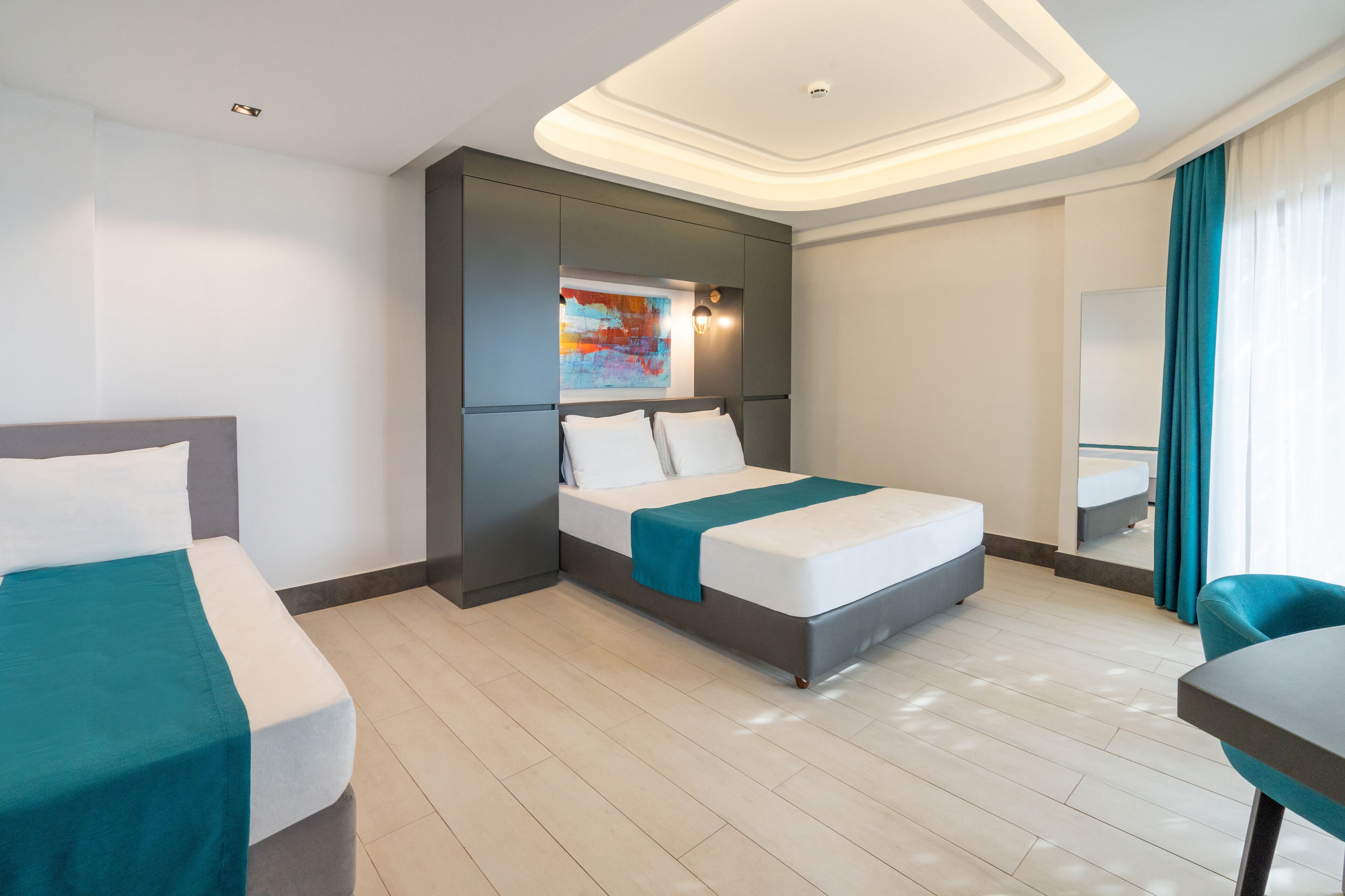 Una habitación de hotel moderna con una cama grande, una cama más pequeña, un escritorio y un espejo de baño.
