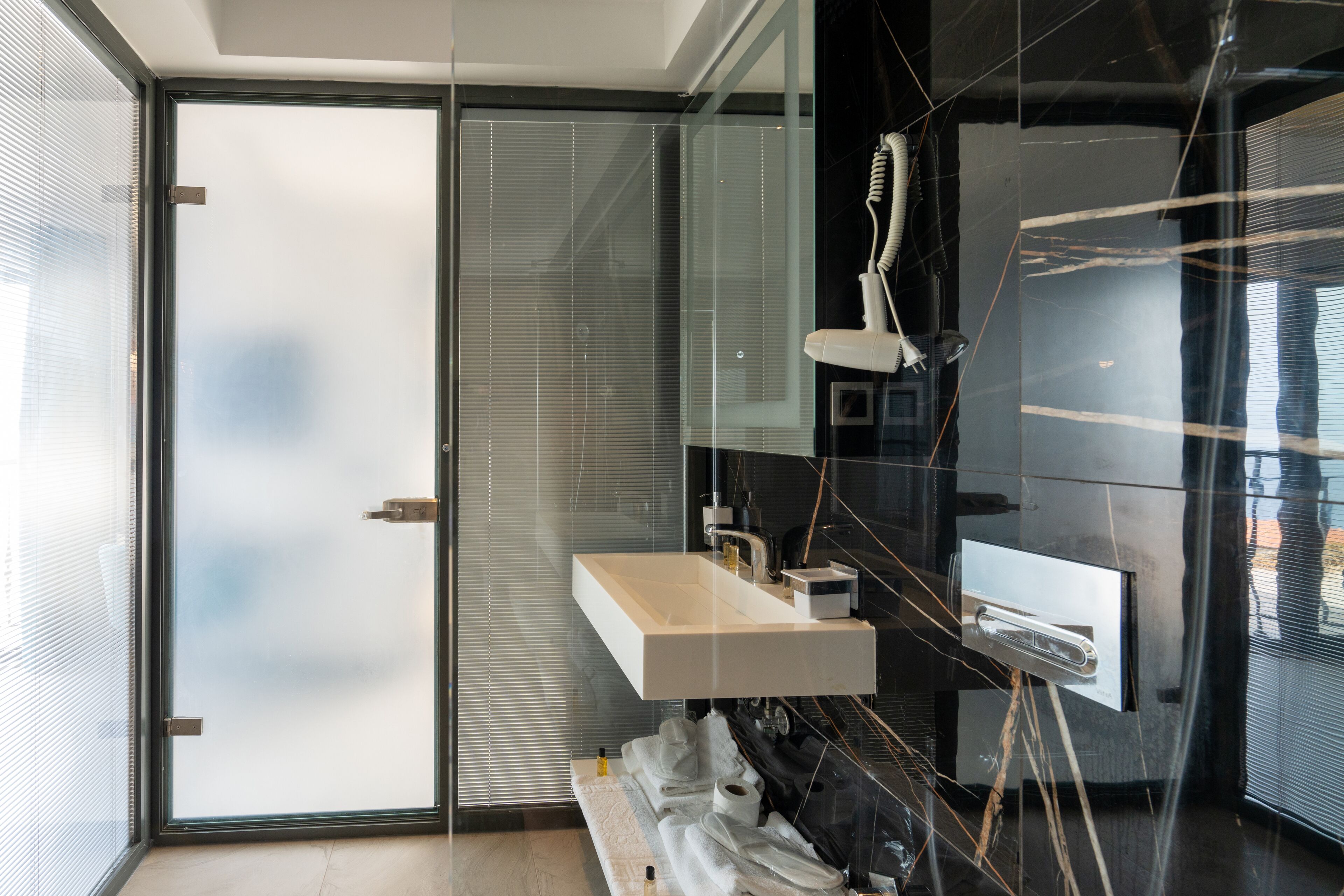 Un baño moderno con puerta de vidrio, un lavabo blanco y un perchero para toallas.