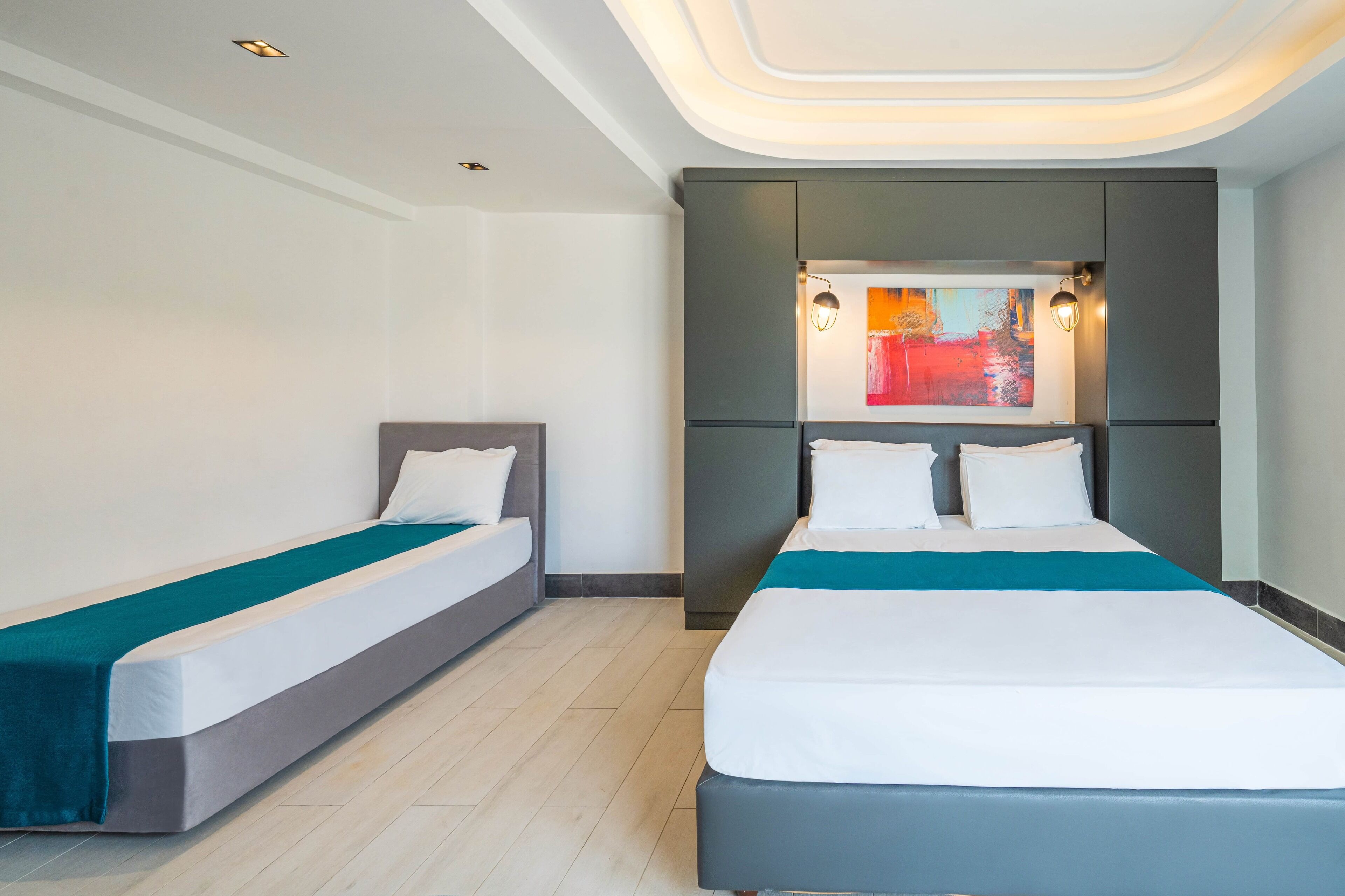 Een hotelkamer met twee bedden, een modern plafondontwerp en een schilderij boven het grotere bed.