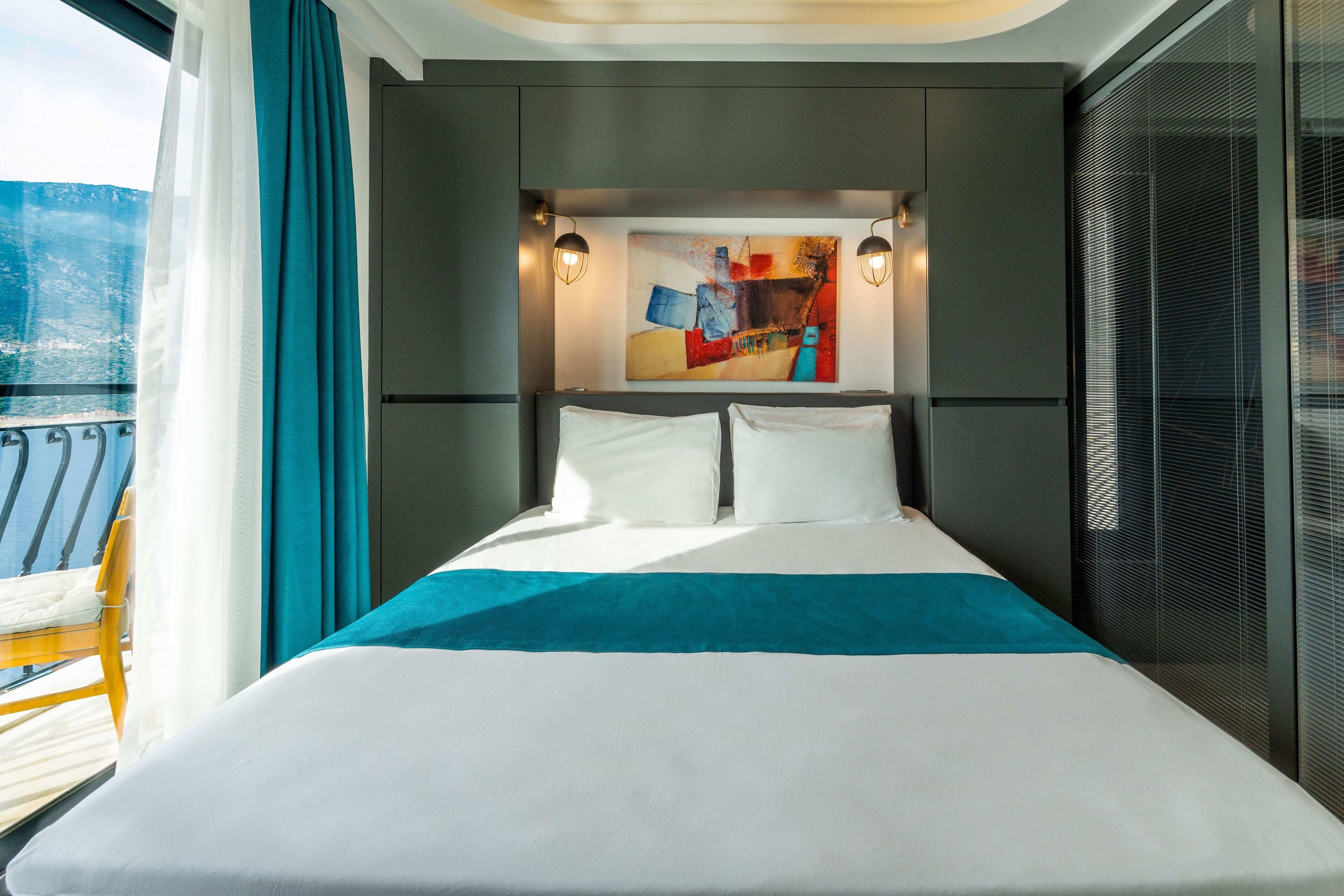 A modern hotel room with a large bed, a view of the sea, and a balcony with a yellow chair.