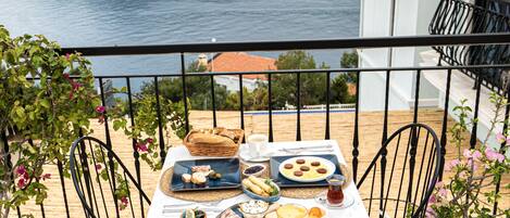 A table set with breakfast items on a balcony overlooking a scenic view of the sea and mountains.