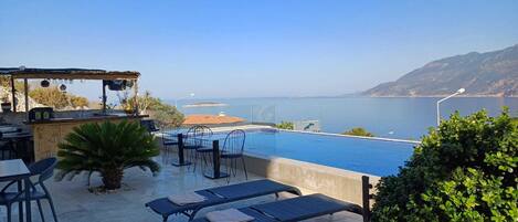 An outdoor pool area with lounge chairs and a barbecue setup overlooking a scenic coastal view.