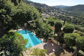 A pool surrounded by lush greenery, with a view of a hilly town in the background. - House with a large pool and a magnificent view (La Londe-les-Maures)