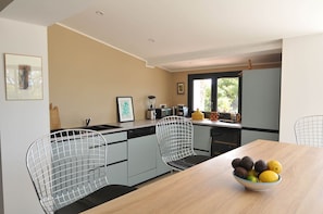 A modern kitchen with a wooden dining table, wire chairs, and a bowl of fruit. - House with a large pool and a magnificent view (La Londe-les-Maures)