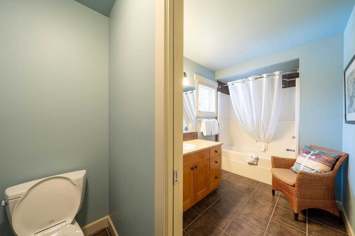 Een badkamer met toilet, wastafel, bad en een rotan stoel.