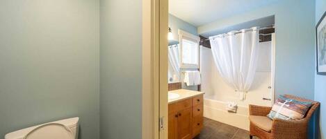 Een badkamer met toilet, wastafel, bad en een rotan stoel.
