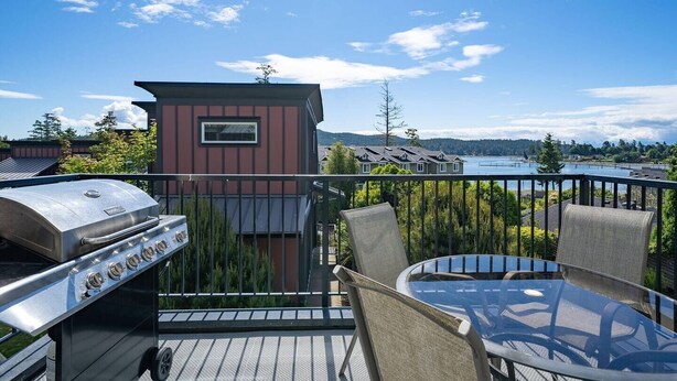 Ein Balkon mit Grill, Stühlen und Blick auf einen See und Häuser.