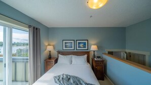 Ein Hotelzimmer mit einem großen Bett, zwei Nachttischen mit Lampen, einem Fenster mit Vorhängen und zwei gerahmten Bildern an der Wand.