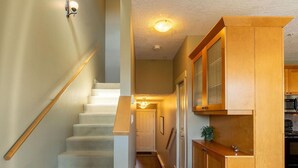 Eine Treppe mit Teppichstufen führt zu einer Zwischenebene. Eine Holzhandlauf ist links, und eine Leuchte an der Wand. Ein Holzkasten mit Glastür befindet sich rechts.