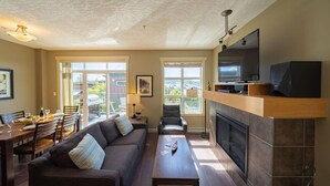 Ein Wohnzimmer mit Sofa, Couchtisch, Kamin, Fernseher und einem Essbereich mit Stühlen und Tisch.