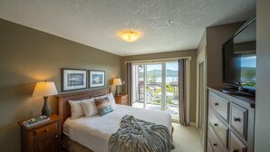 A hotel room with a bed, bedside lamps, a television, a dresser, and a balcony with a view of the outdoors. - 2 Bedroom Sooke Townhome (Sooke)