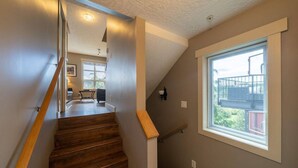 Eine Treppe mit Holzboden und Geländer, die zu einem Zimmer mit großem Fenster und Balkonblick führt.