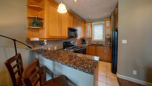 A kitchen with wooden cabinets, granite countertops, a black microwave, and a refrigerator.
