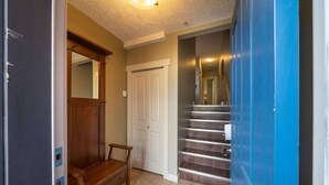 A hallway with a wooden bench, a white door, and a staircase with metal railings.