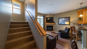 A staircase leading to a living area with a fireplace, a television, and a dining area with chairs.