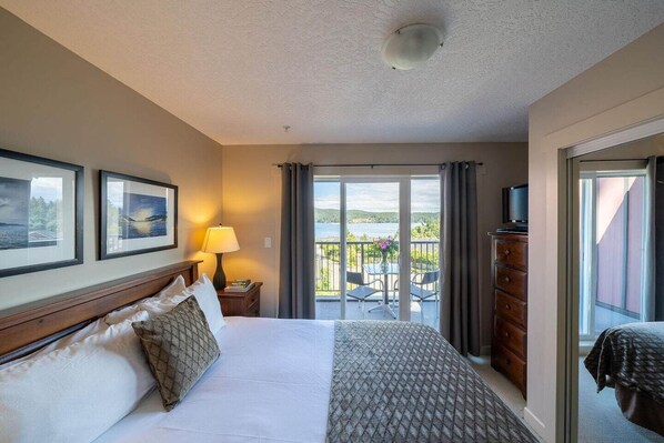 A hotel room with a bed, a nightstand, a lamp, a dresser, and a balcony with a view of the outdoors.