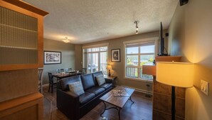 A living room with a black leather sofa, a dining table, and a TV. - 3 Bedroom Sooke Townhome (Sooke)