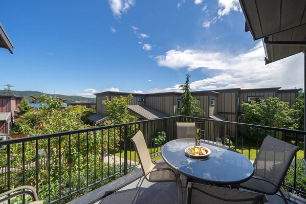 A balcony with a round table and chairs, a bottle of wine, and a plate of food. - 3 Bedroom Sooke Townhome (Sooke)