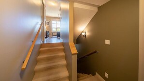 A staircase with wooden handrails and carpeted steps leading to a room with a window and a wall-mounted light fixture. - 3 Bedroom Sooke Townhome (Sooke)