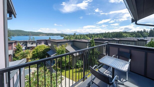 A balcony with a table and chairs, overlooking a lake and forested hills. - 3 Bedroom Sooke Townhome (Sooke)
