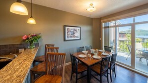 A dining area with a wooden table set for four, a granite countertop, and a large window offering a view of the outdoors. - 3 Bedroom Sooke Townhome (Sooke)