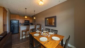 A modern kitchen with wooden cabinets, a black refrigerator, and a dining area with a wooden table set for four.