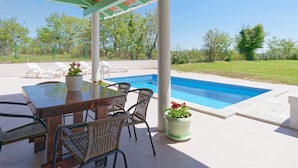 Un espacio exterior techado con piscina, una mesa con sillas y plantas en macetas.