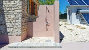 Un edificio de piedra con zona de ducha, una ventana de madera y calentador solar de agua.