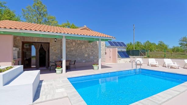 Una piscina con un edificio de piedra y paneles solares al fondo.