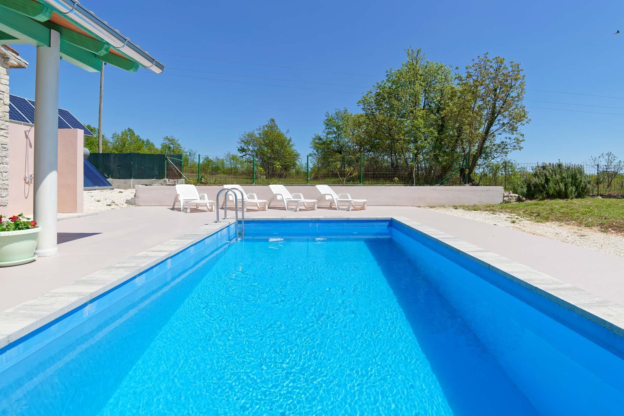 A swimming pool with lounge chairs, a covered area, and a clear sky.
