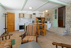 A compact kitchen with wooden cabinets, a dining area with striped chairs, and a stone wall. - Holiday Home Gimino - Two Bedroom Holiday Home with Pool (Zminj)