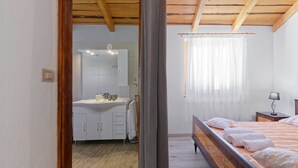 Un dormitorio con una cama de madera, una mesita de noche y un ventanal con cortinas traslúcidas.