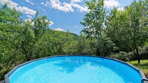 A swimming pool surrounded by lush greenery and trees, with a clear blue sky above. - Casa Mira - Two Bedroom Holiday Home with Pool (Pazin)