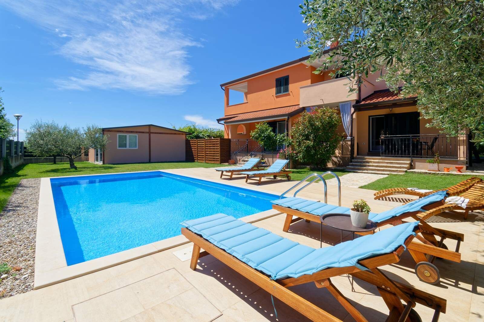 Une piscine avec des chaises longues, une petite maison et un arbre.