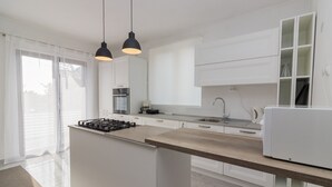 Una cucina moderna con mobili bianchi, un'isola centrale, un piano cottura e luci a sospensione.