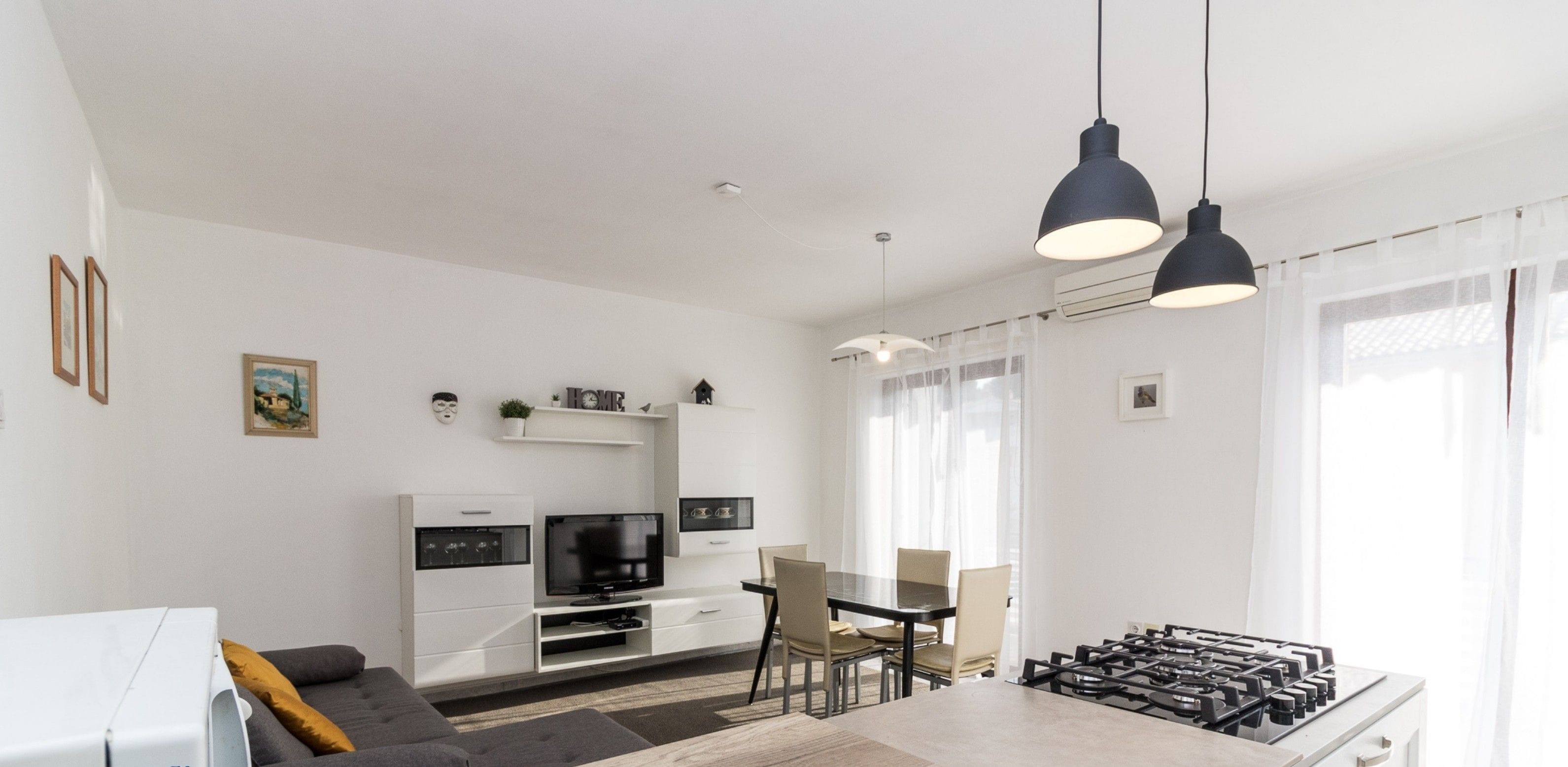 A modern kitchen with a central island, dining area with chairs, and a TV in the background.