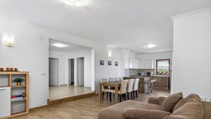 A modern living room with a sofa, a dining table, and a kitchen in the background. - Apartments Belvedere-Three Bedroom Apartment with Balcony (Buje)