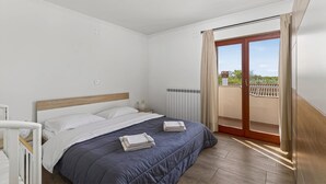 A bedroom with a bed, a nightstand, a radiator, and a view of the outside. - Apartments Belvedere-Three Bedroom Apartment with Balcony (Buje)