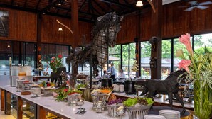 A buffet setup with various food stations, a decorative horse sculpture, and a view of the outdoors through large windows. - Phumontra Resort Nakhon Nayok (Nakhon Nayok)